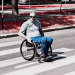 Hombre en silla de ruedas cruza una calle usando una rampa de banqueta en una zona urbana.